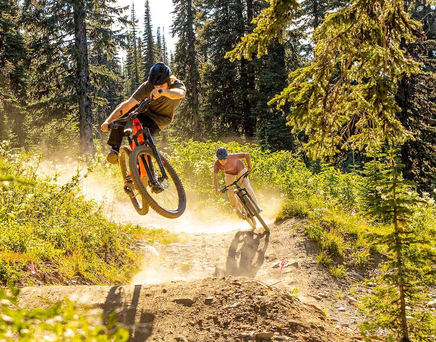 2 mountain bikers riding the 5010 off of a jump in the forest